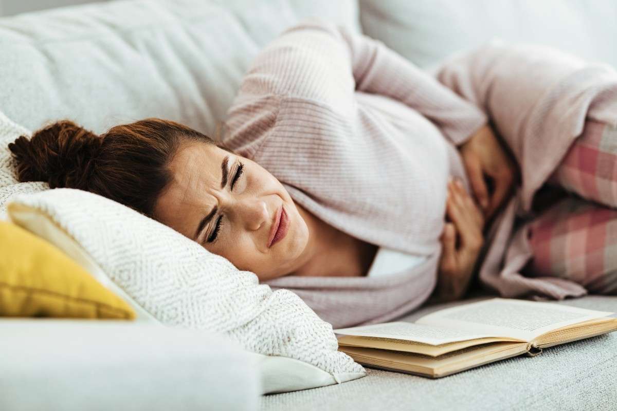 Women lying on a couch with a book groaning in pain