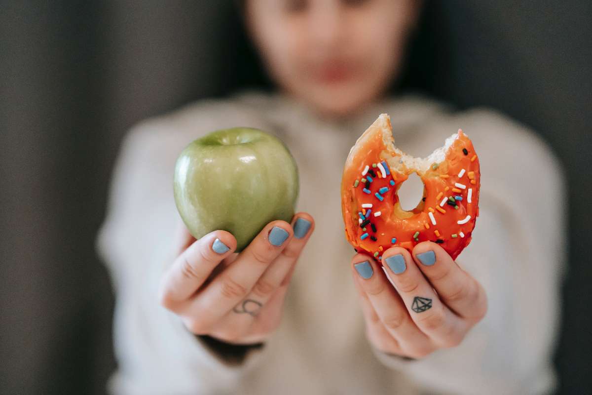 A girl holding a healthy snack in one hand and junk in the other shows the difference between appetite and hunger