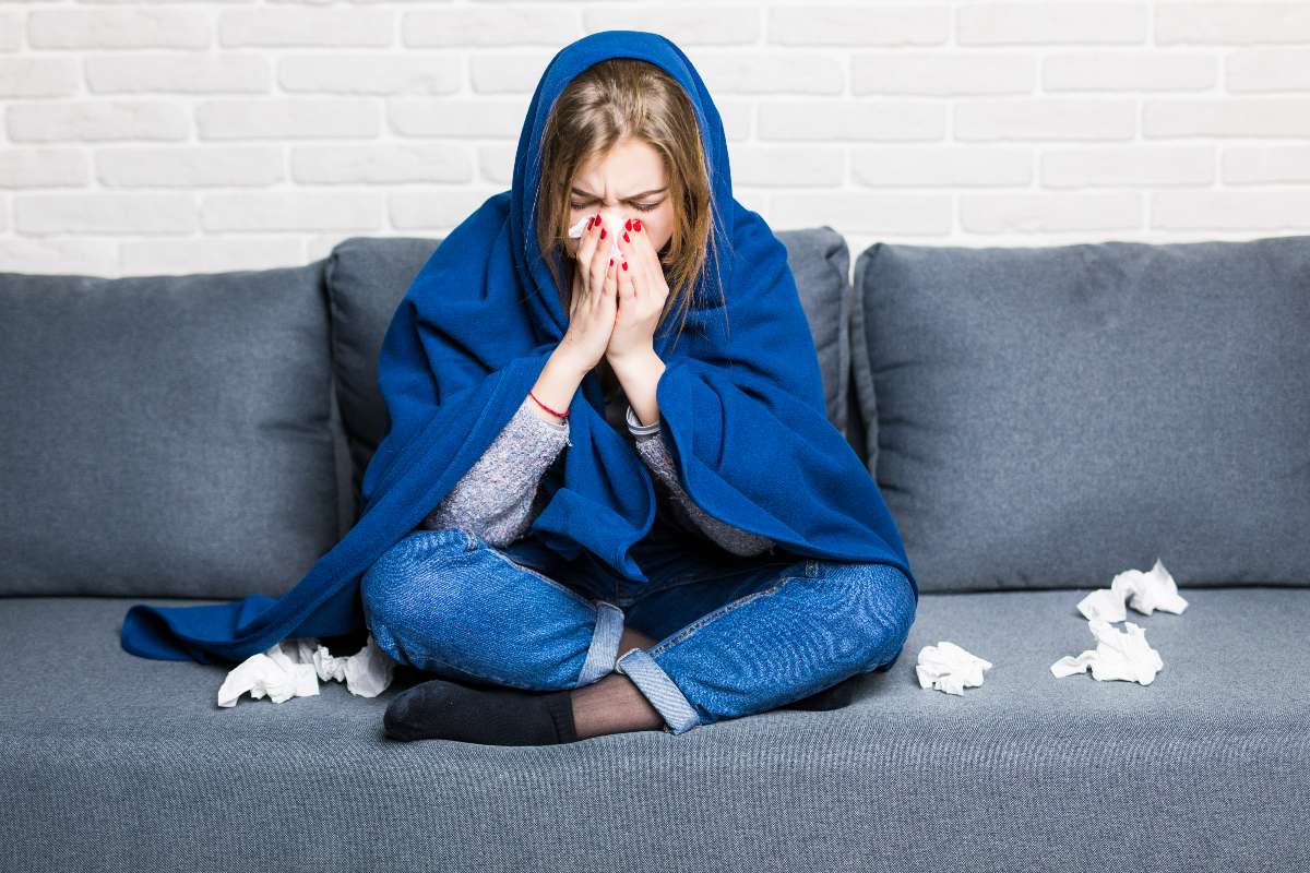 A women suffering from common cold holding napkin and covered in a blue blanket.