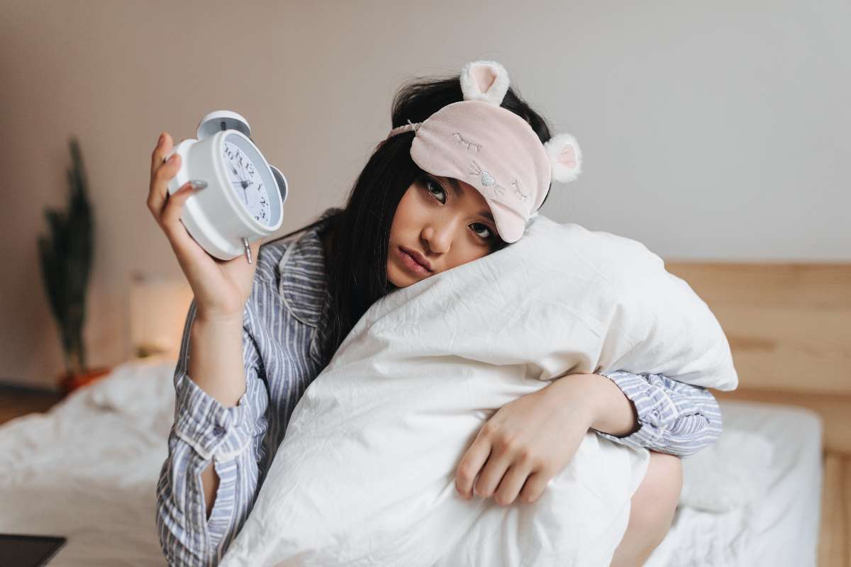 A young girl holding a clock and getting ready to sleep suffering from Insomnia