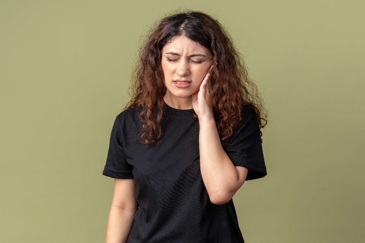 A girl with curly hair experiences a common tooth cavity symptom called toothache.