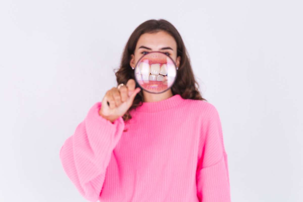 A girl holding a Magnifying glass in front of her teeth showing Toothache Symptom